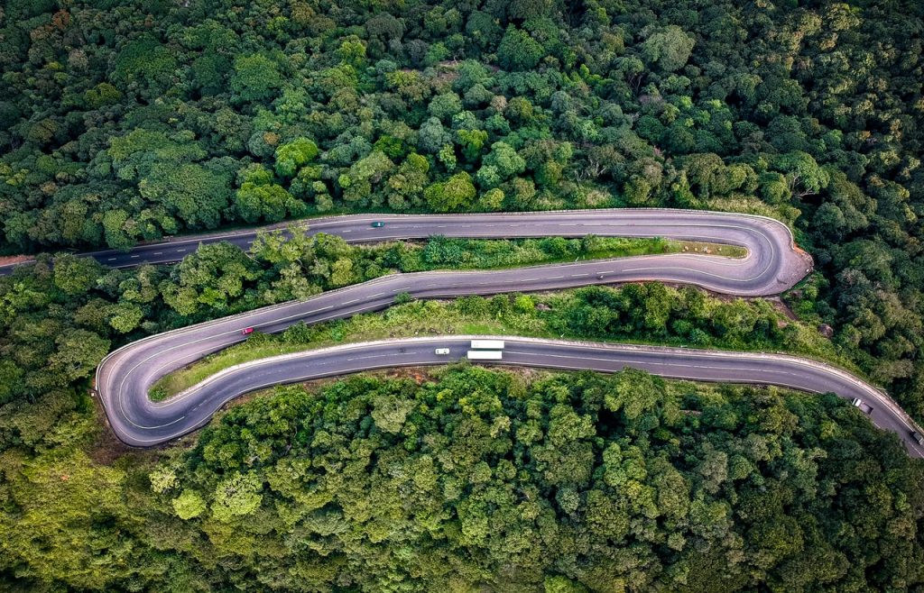 Birds eye view of road with tight hairpins, threading through dense forest